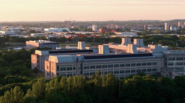 Aerial view of the GSK research facility and modern laboratory buildings surrounded by green trees during golden hour in Stevenage, England, United Kingdom.