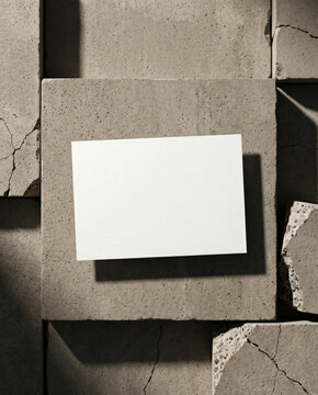 Blank white card mockup on raw concrete slabs with cracked stone fragments, minimal brutalist copy space background