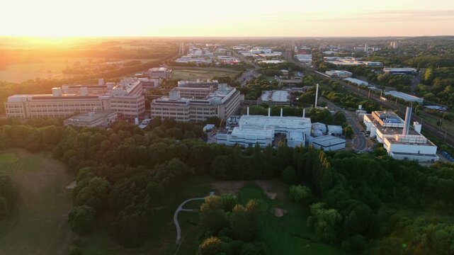 Aerial view of the GSK Stevenage research and development campus during golden hour with modern buildings surrounded by lush green trees in Stevenage, England, United Kingdom.