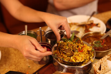 Naklejka na ściany i meble Close Up of Hands Serving Traditional Indian Lamb Biryani at Restaurant