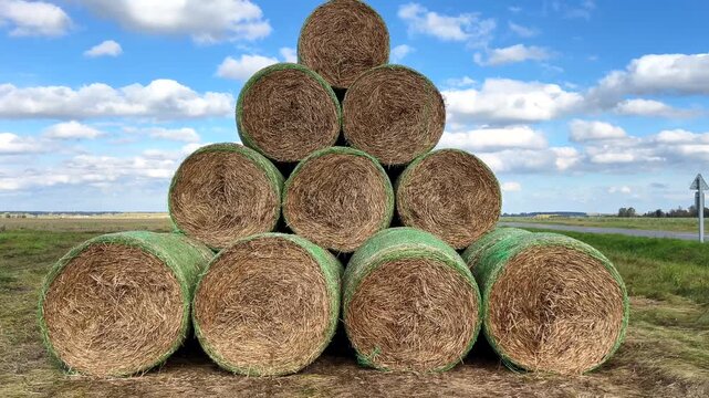 Round hay bales stacked in pyramid in a field with blue sky and white clouds
