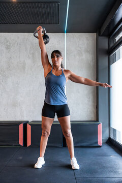 Woman lifting kettlebell overhead in modern gym setting