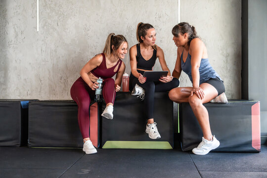 Three women review workout plan on tablet in gym