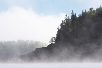 Fog drifting over rocky Bureya Reservoir shoreline with sparse trees and a soft morning atmosphere © Mikhail Mishchenko