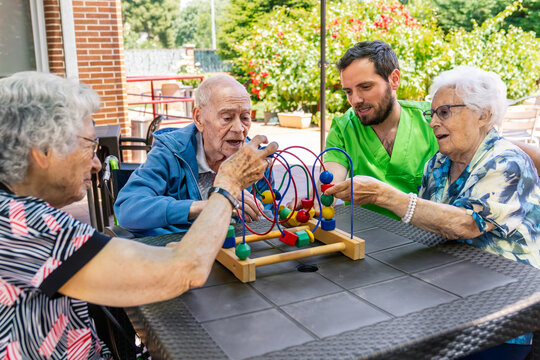 Caregiver assisting elderly residents playing a bead maze puzzle for occupational therapy and cognitive stimulation in an outdoor area