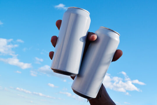 Hand holding two cans against sky