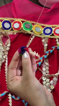 Close-up of hands stitching a colorful pompom embellishment onto a handcrafted costume, showcasing traditional textile craftsmanship, embroidery techniques, and artisan fashion detailing.