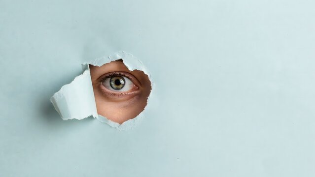 Peeking eye through torn paper hole curiosity concept