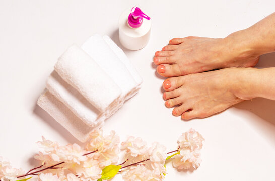 High angle view of female feet prepared for a professional pedicure treatment, clean white towels, dispenser bottle and pink cherry blossoms nearby.Top view of bare woman feet 