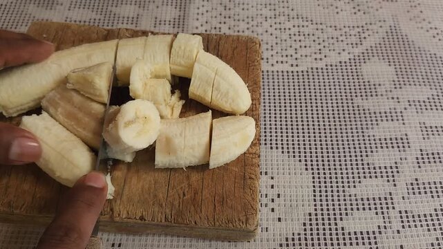 Hand Cutting Slices of Ripe Tabasco Banana on Wood Board with Knife