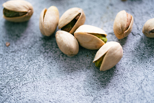 Whole roasted pistachio nuts in shells scattered on a blue textured background,Close-up of salty organic pistachios in shell, healthy vegan snack food concept