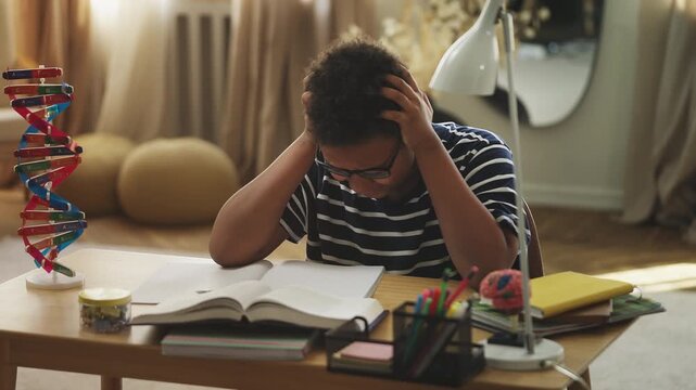 Exhausted African American boy holding his head while preparing for a test