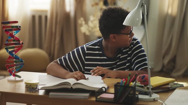 Tired African American boy holding his head while studying in a noisy room