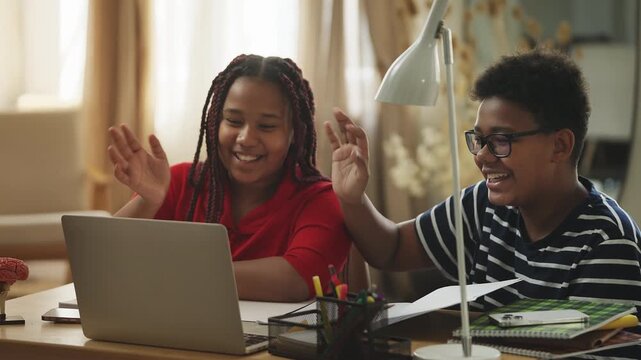 Smiling African American siblings waving at the camera during an online lesson