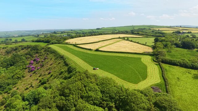 Approaching Aerial View of Agricultural Tractor Machine mowing Vibrant Green Field in English Countryside in Spring. Agricultural industries, commercial landscaping, rural lifestyle. 4K.
