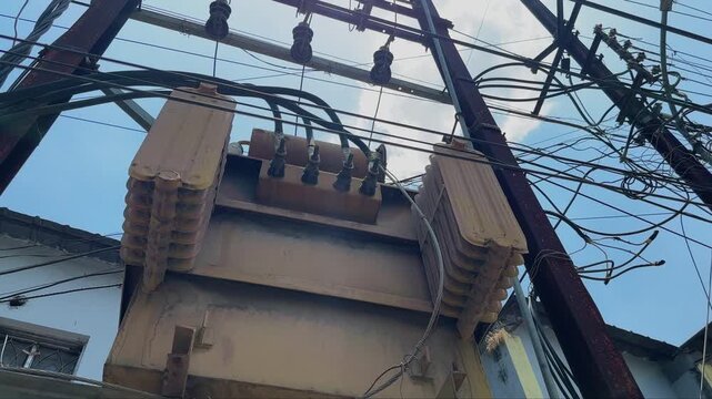 Camera orbiting around a pole mounted electrical distribution transformer with overhead power lines, insulators and utility cables against a bright daytime sky in an urban setting.