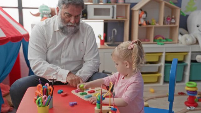 Man and little girl at a red table, girl handing a wooden shape block to the man's hand in a preschool building; gentle care.