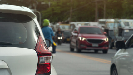 Naklejka premium Behind a white car driving on the asphalt road. Cars drive past on the road with motorcycles leading the way. Passenger cars are lined up in a long queue. Background of trees side road.