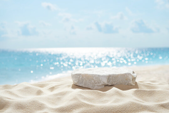 Tropical stone podium on summer beach sand with blurred sunlit sea and sky background