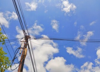 Fototapeta premium Utility pole with tangled power lines against a blue sky with white clouds