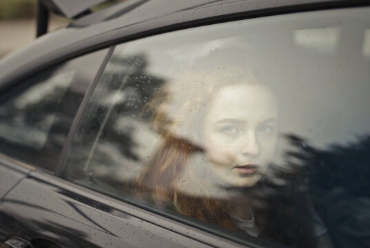 Pensive young woman staring through a rainy car window