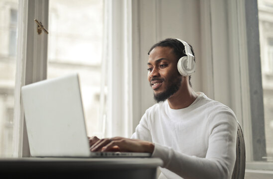 Smiling man with headphones types on laptop computer