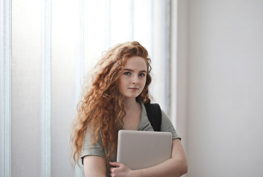 Confident young student with curly red hair holds a laptop