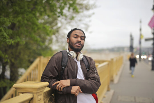 Young Black man with headphones posing on a city bridge