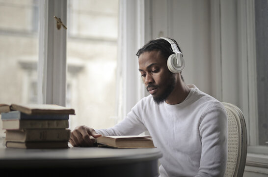 Young man reads a book while wearing headphones