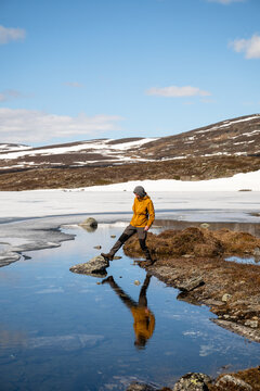 Hiker crossing meltwater beside frozen lake in Lapland Finland