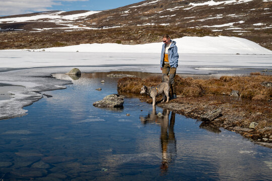 Woman and her dog pause by a clear mountain lake in Lapland Finland