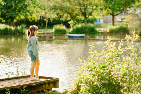 Child girl standing quietly on lakeside dock surrounded by nature