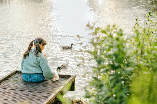 Girl sitting on a wooden dock feeding birds on a lakeside pond