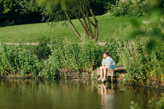 Child girl sitting on wooden dock beside calm lake in summer