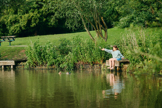 Girl feeding waterfowl while sitting on a dock by a lake