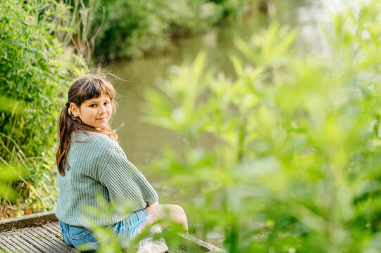 Portrait of a girl sitting beside a lake surrounded by greenery