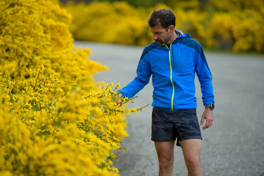 Man stops on his run to admire yellow flowers