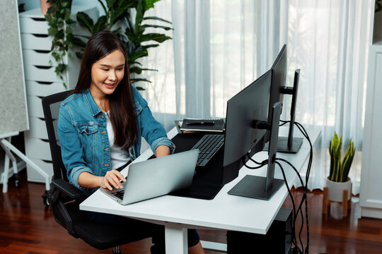 Smiling young Asian in IT developer creating with typing online information on laptop with coding program data of application, wearing jeans shirt. surrounded by safety analysis two screen. Stratagem.