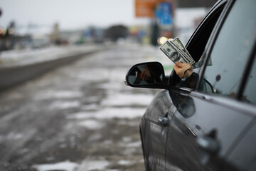 Naklejka premium Hand Holding Dollar Bills Out of Car Window on a Cold Snowy Day