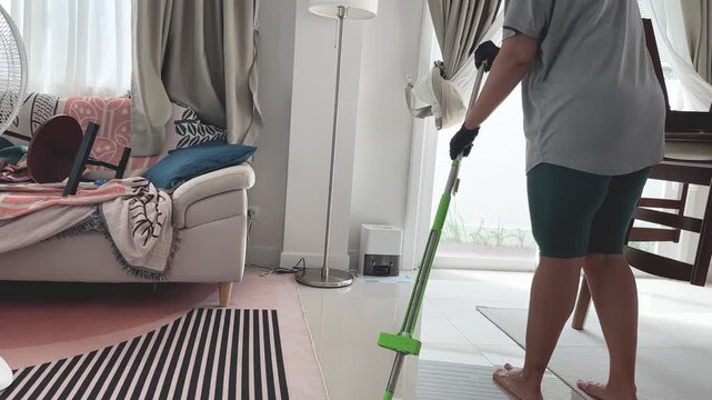 Woman mopping a tiled floor in the living room, everyday home cleaning and housekeeping routine in a modern apartment interior.