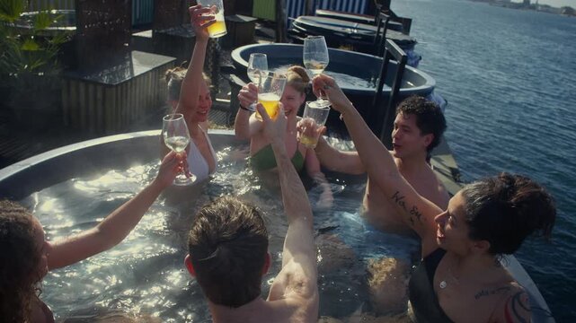 Friends relaxing in outdoor hot tub and toasting drinks by the waterfront