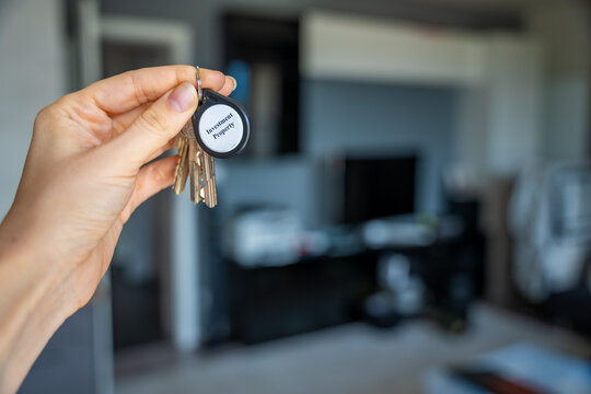 Woman holding house keys with investment property keychain inside modern apartment interior. Real estate investment and property ownership concept for passive income and wealth building