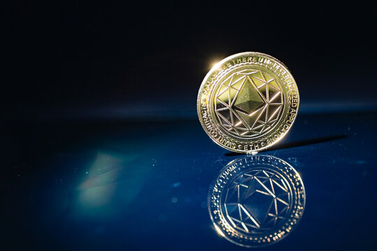  Moneda f&iacute;sica Ethereum ETH de oro con reflejo en una superficie oscura de color azul intenso, fotograf&iacute;a editorial.