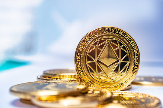  Moneda f&iacute;sica Ethereum ETH de oro inclinada sobre monedas de oro dispersas sobre un fondo azul claro,
Imagen editorial de tono brillante de la moneda Ethereum para noticias sobre el aumento de precio