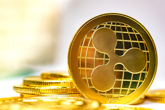  Moneda f&iacute;sica Gold Ripple XRP colocada sobre una pila de monedas con un fondo c&aacute;lido de luz amarilla dorada, imagen editorial c&aacute;lida de la moneda Ripple XRP para noticias de corridas alcistas de XRP,