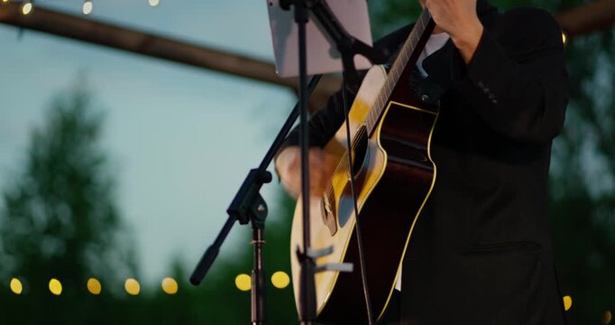 Close-up of musician strumming acoustic guitar on outdoor dusk stage