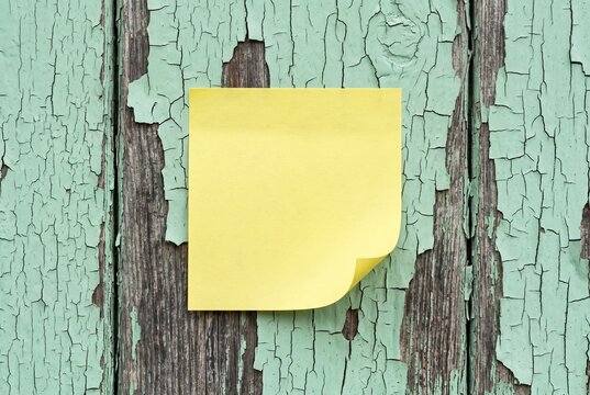 Blank yellow sticky note on vintage weathered wood wall with cracked pastel mint green paint, copy space mockup