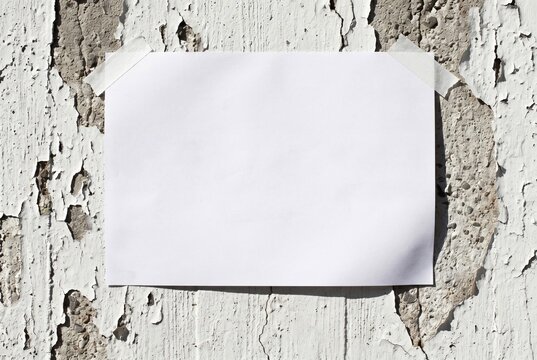 Blank white paper note taped on rustic peeling paint wall, copy space mockup, grunge texture background