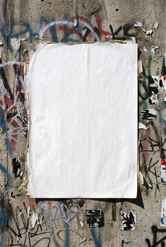 Blank white poster paper glued on urban concrete wall with graffiti and street art, copy space mockup
