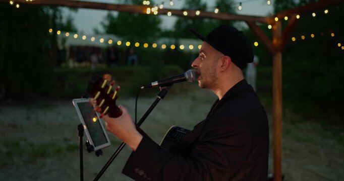 Male Singer Guitarist Performing on Dimly Lit Outdoor Stage at Dusk